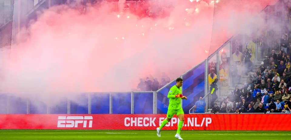 Goalkeeper walking past smoke and flares in stadium