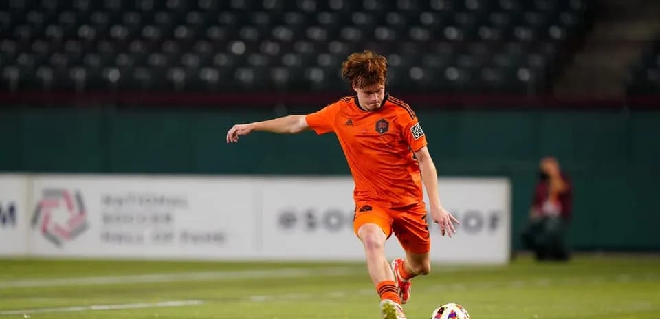 Player in orange jersey kicking soccer ball