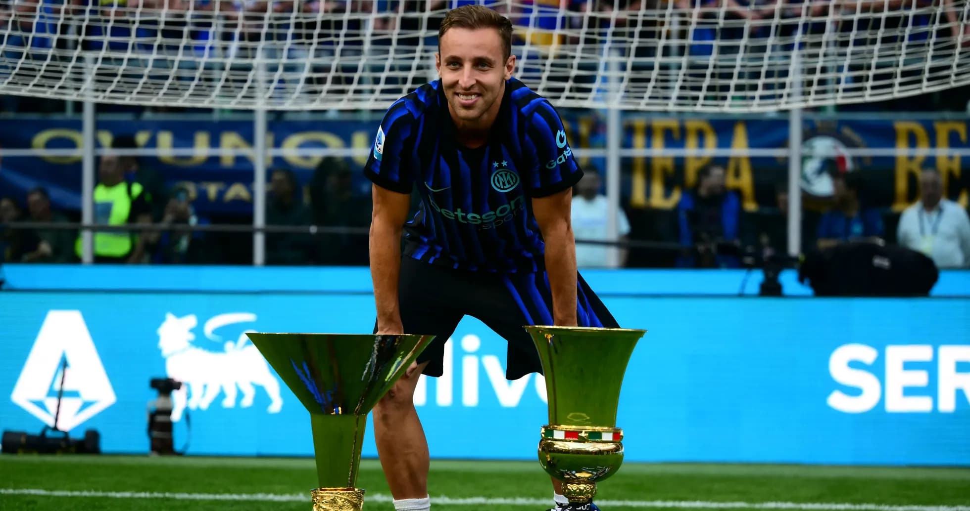 Player posing with two trophies on the field