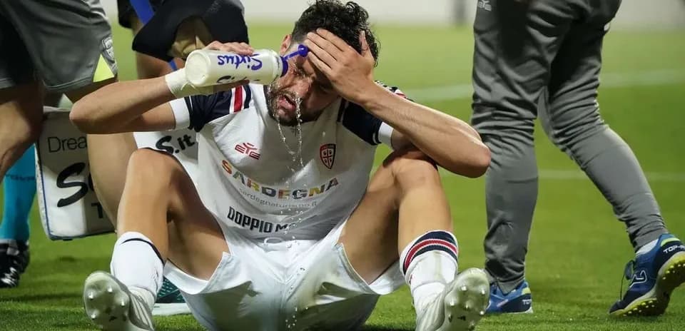 Player sitting on pitch pouring water on forehead