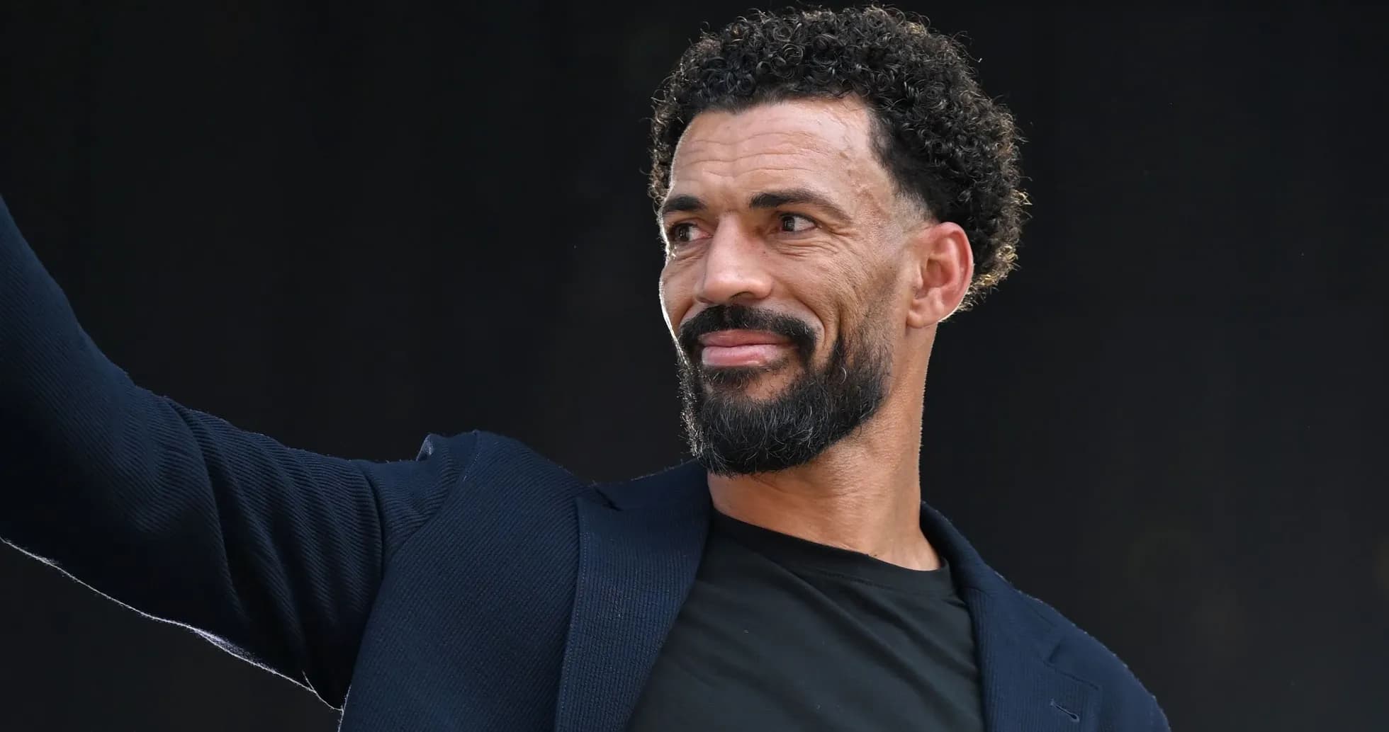 Man waving while wearing a dark blazer