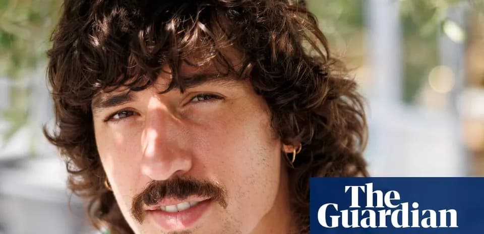 Man with curly hair and mustache smiling outdoors
