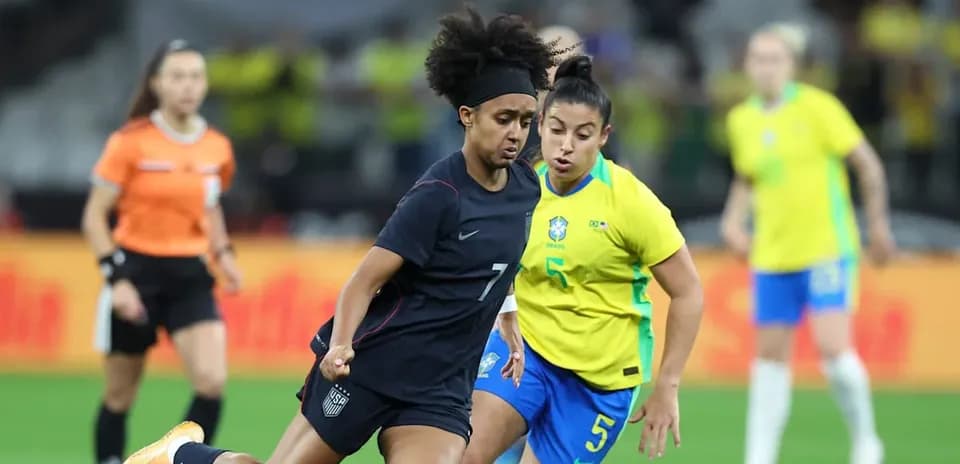 US player dribbling past Brazilian defender in match