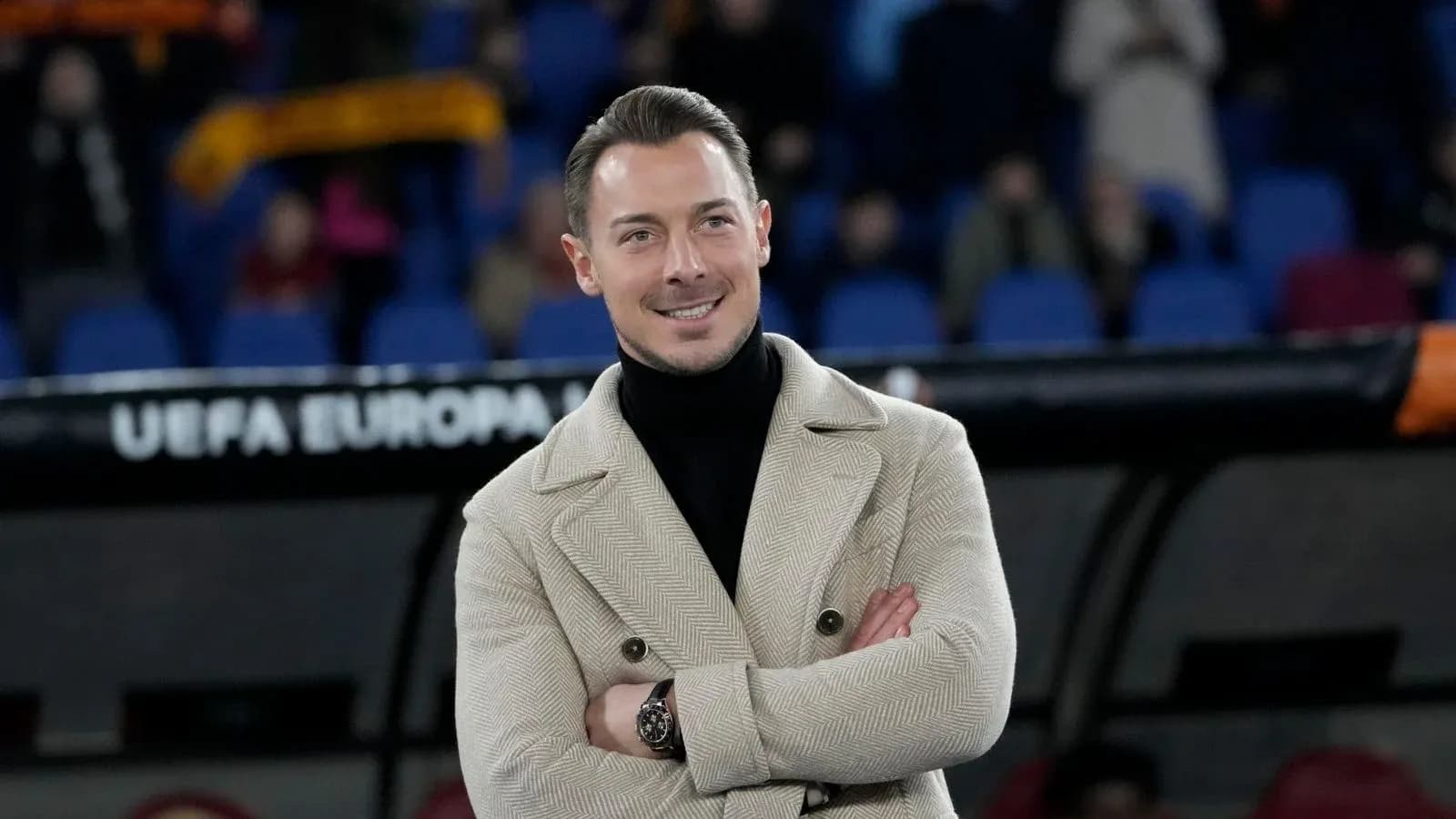 Man in stylish coat smiling at stadium