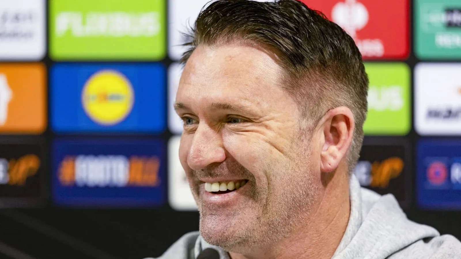 Man smiling during a press conference backdrop