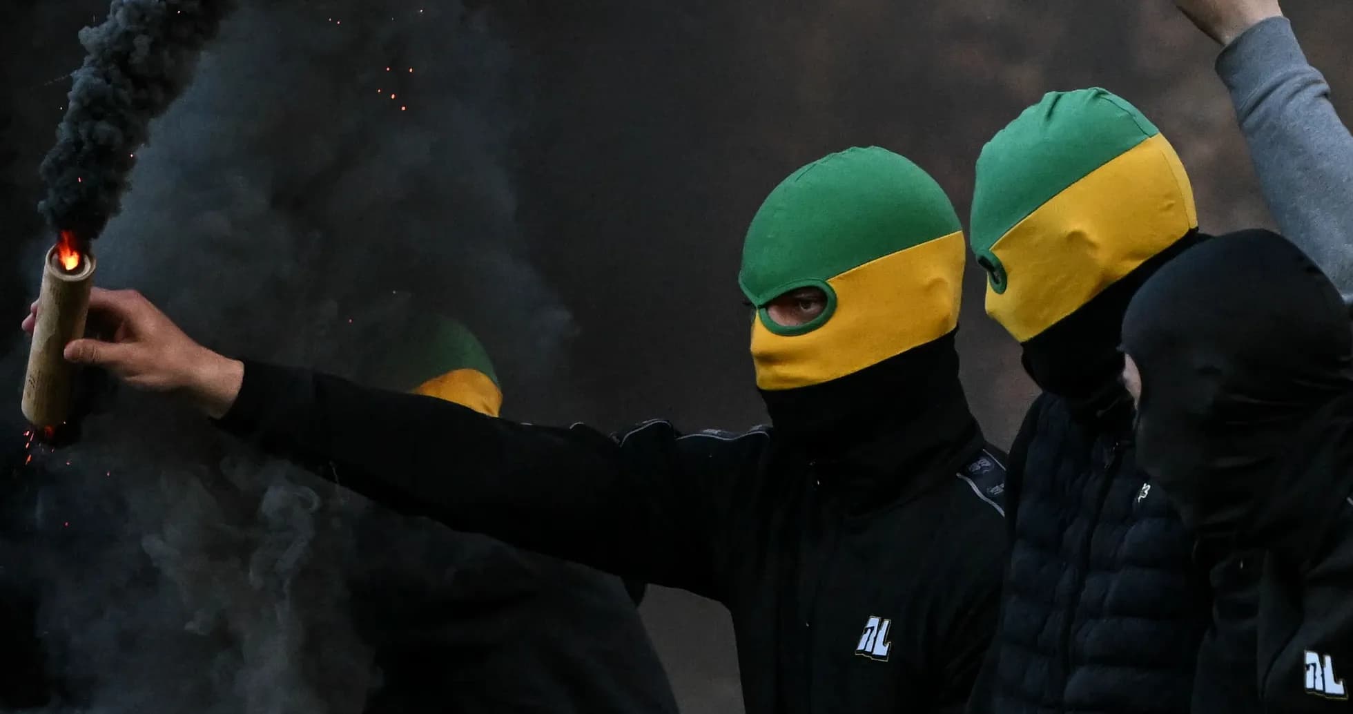 Masked individuals holding a flare in smoky environment