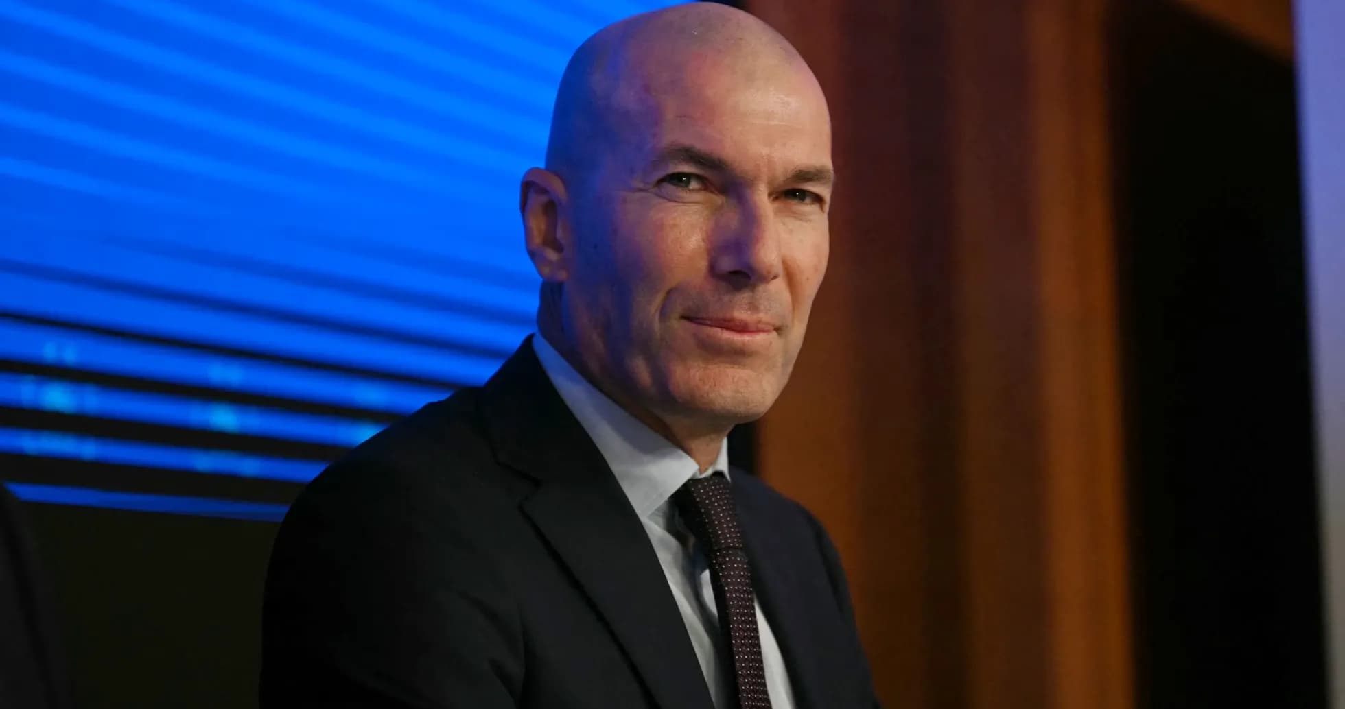 Man in suit at press conference with blue backdrop