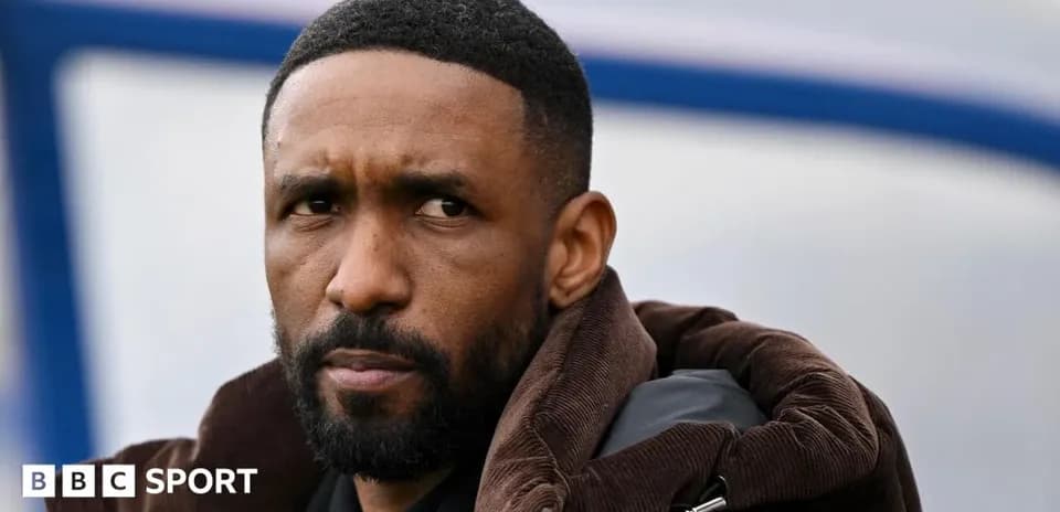 Man with beard wearing a brown jacket, looking thoughtfully