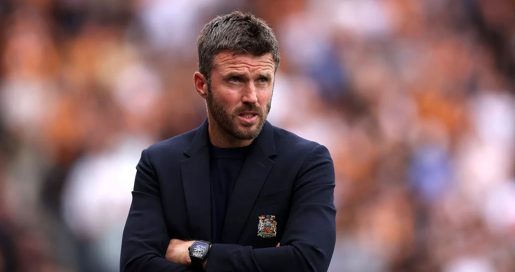 Coach standing with arms crossed during match