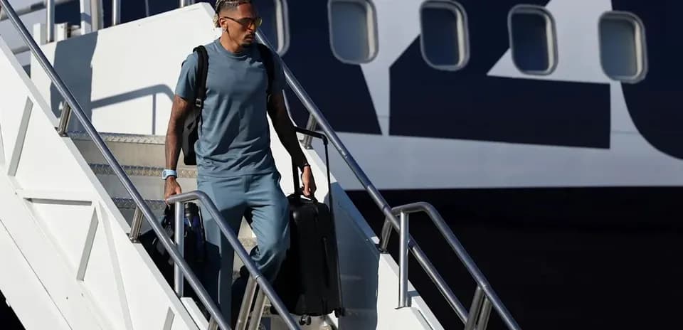 Player exiting airplane with suitcase at airport