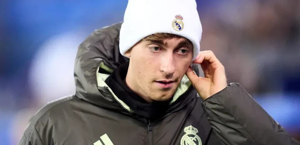 Player wearing Real Madrid jacket and beanie on pitch