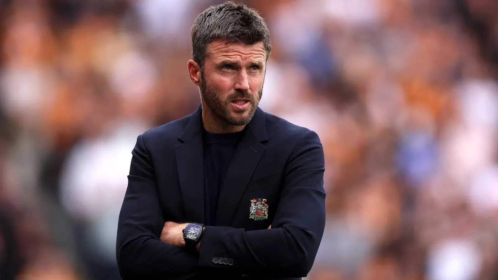 Coach standing with arms crossed during match