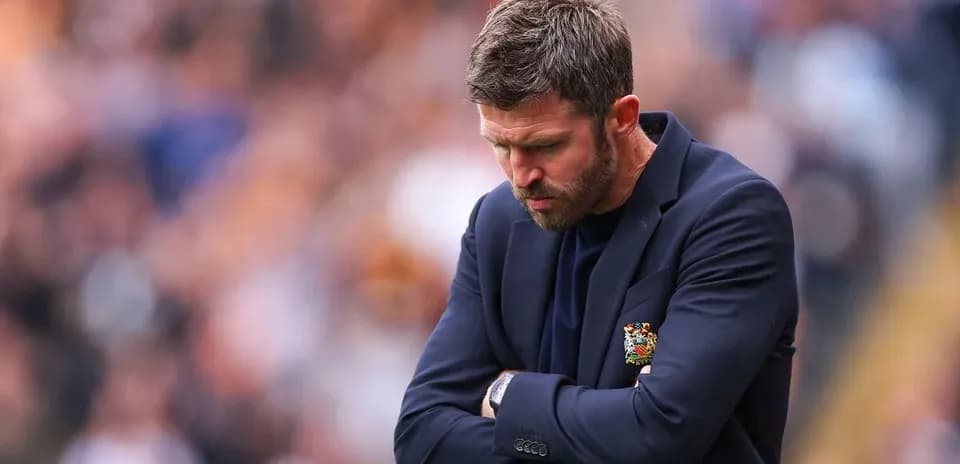 Manager with arms crossed looking down during match