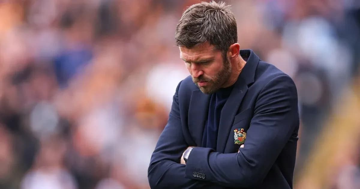 Manager with arms crossed looking down during match