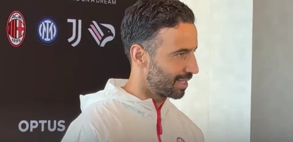 Man speaking at press conference with club logos