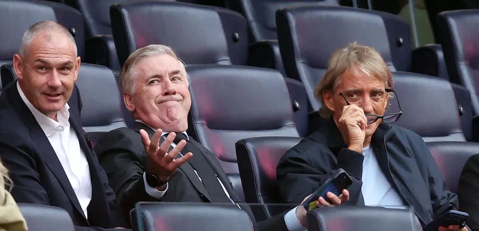 Three men seated in stadium, engaging in conversation