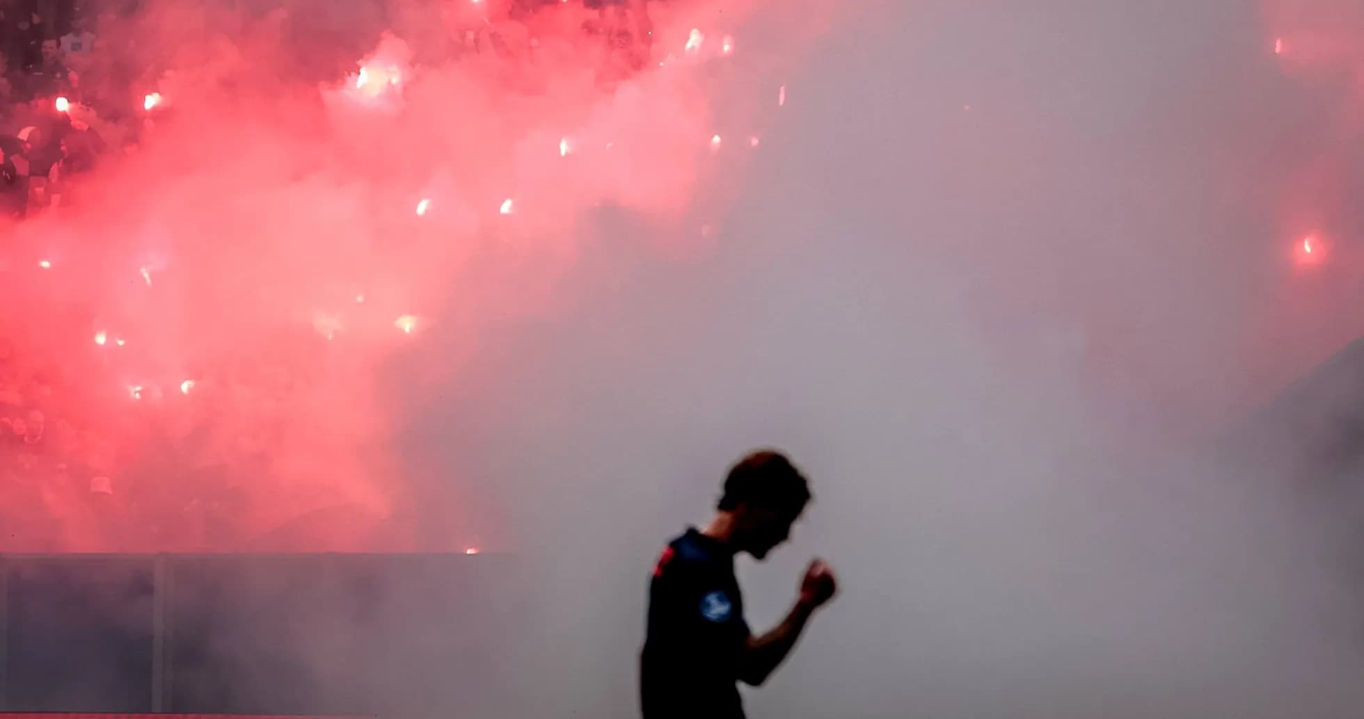 Player celebrating amidst smoke and flares in stadium