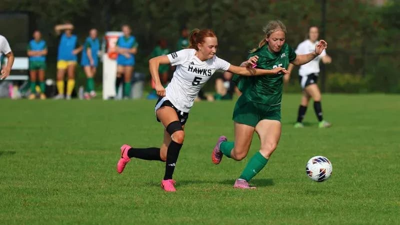 Player in black chasing ball from opponent in green
