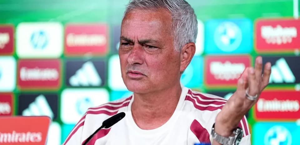 Manager speaking at press conference with logos in background