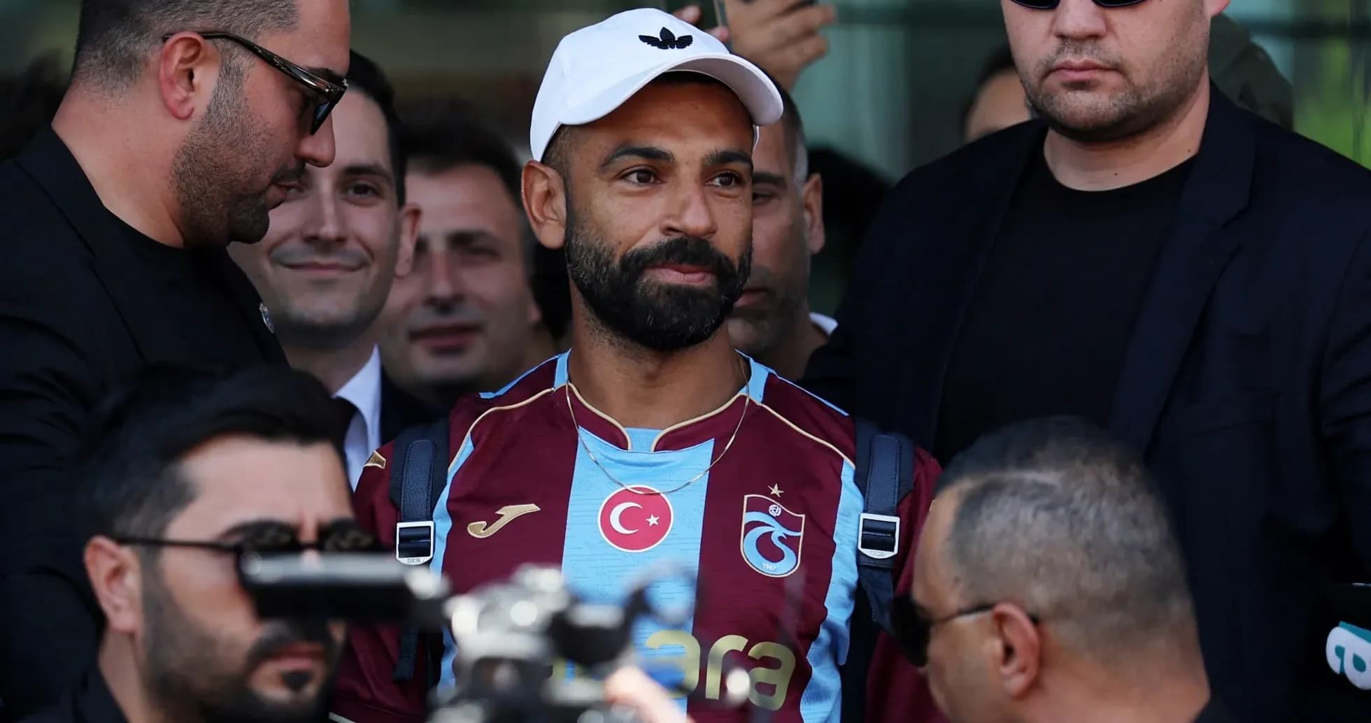 Player in Trabzonspor jersey surrounded by security personnel Player in Trabzonspor jersey surrounded by security personnel
