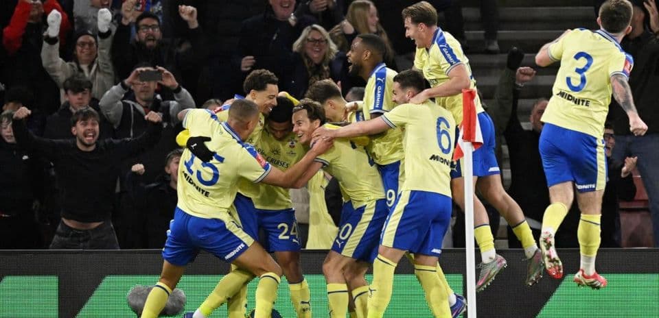 Players celebrating a goal with fans in background Players celebrating a goal with fans in background