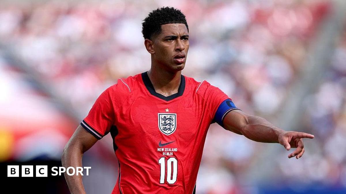 Player in red England jersey directing teammates on field Player in red England jersey directing teammates on field
